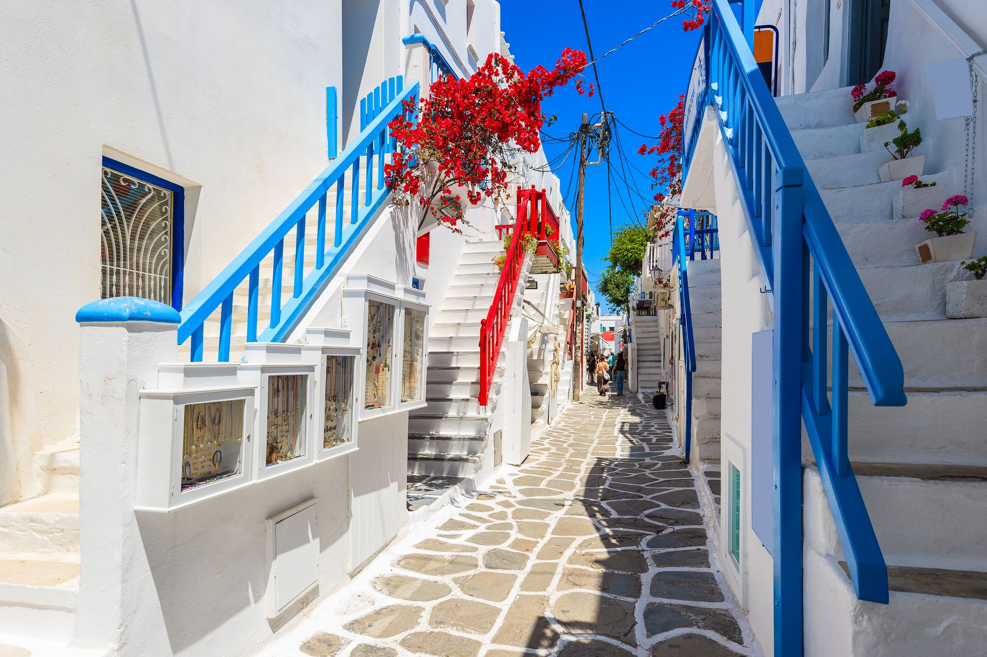 A whitewashed lane in Chora with blue railings, stone paving and bougainvillea